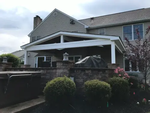 Covered patio with greenery and brick wall.