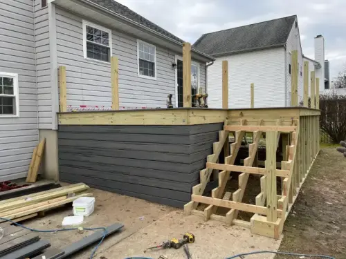 Partially constructed wooden deck with stairs, house background.