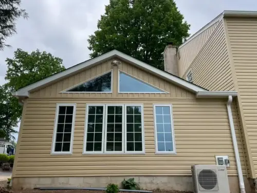 Beige house exterior with large windows and tree backdrop.